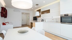 Et moderne køkken med hvide skabe, indbygget ovn og spiseplads med et hvidt bord og stole.