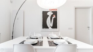 Et spiseområde med et hvidt bord dækket til to personer, et indrammet plakat på væggen og en moderne lampe over bordet.