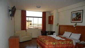A hotel room with a bed, a desk, a chair, a wooden cabinet, and a window with curtains. - Hotel Moquegua (Moquegua)