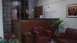 A reception area with a wooden desk, red leather chairs, a small side table, and a potted plant. - Hotel Moquegua (Moquegua)