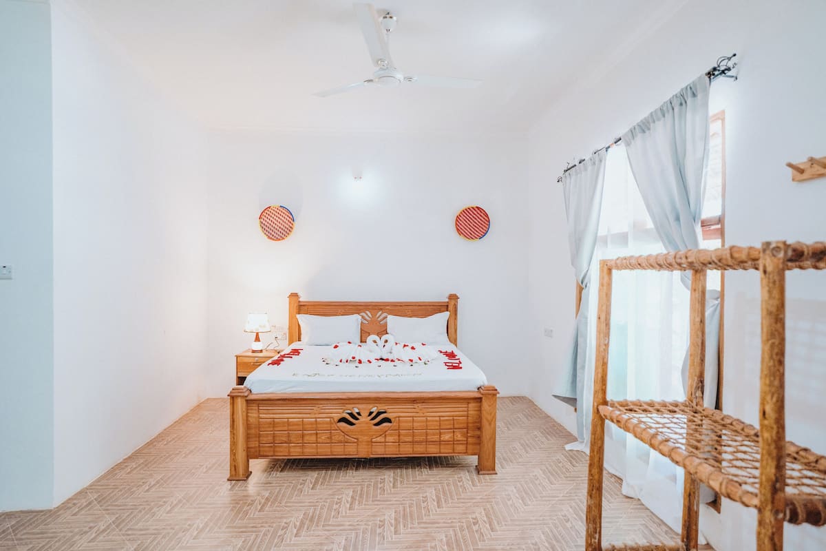 Ein Schlafzimmer mit einem hölzernen Bett, einem Nachttisch mit Lampe, einem Deckenventilator und einem Fenster mit Vorhängen.