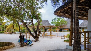 A beachside resort with thatched-roof huts, wooden lounge chairs, and a sandy walkway. - Bella Vista Resort Zanzibar (Kizimkazi)