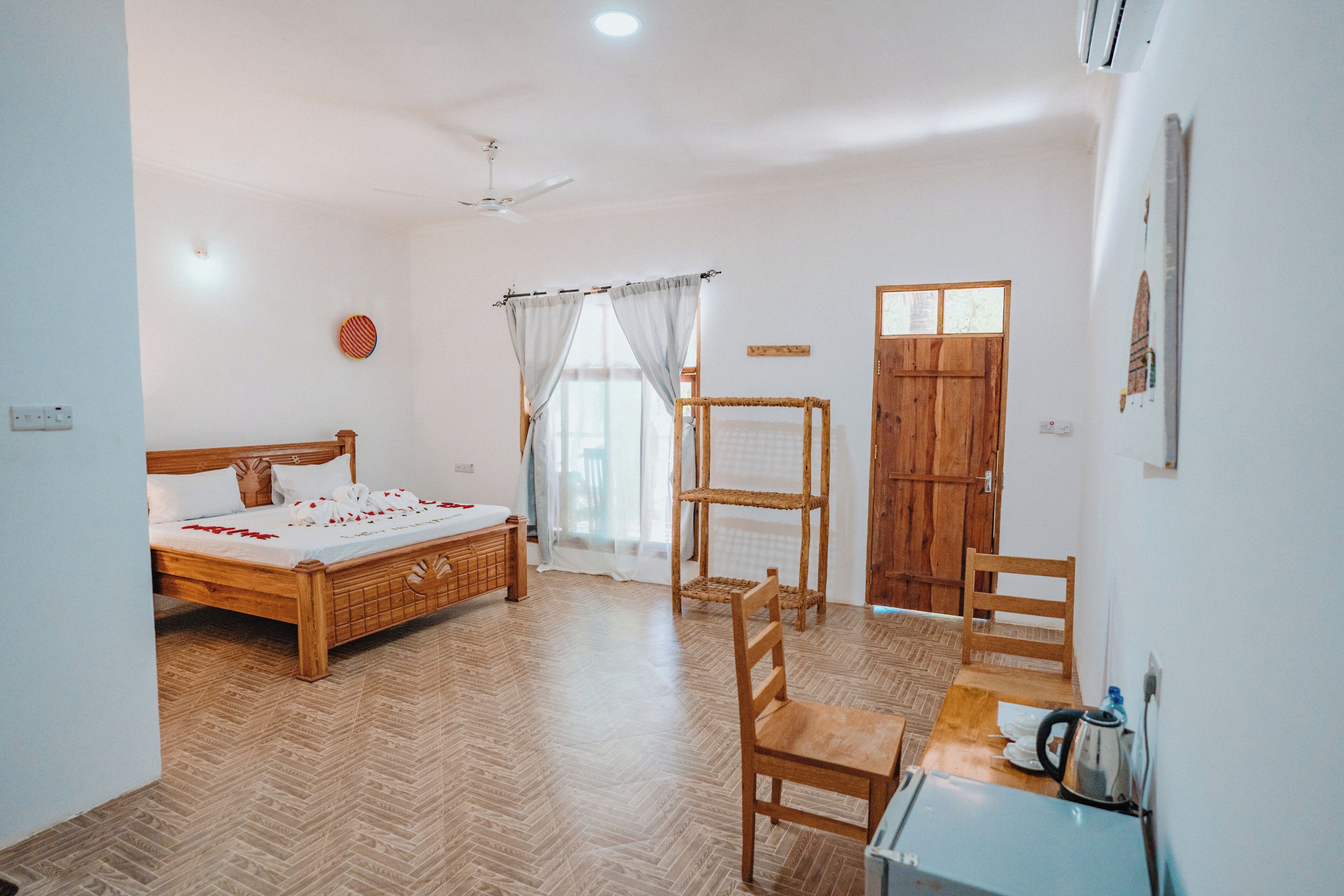 Quarto com cama de madeira, uma cadeira, uma mesinha, radiador e porta.