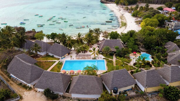 A resort with thatched-roof bungalows, a central pool, and a beach with boats. - Bella Vista Resort Zanzibar (Kizimkazi)