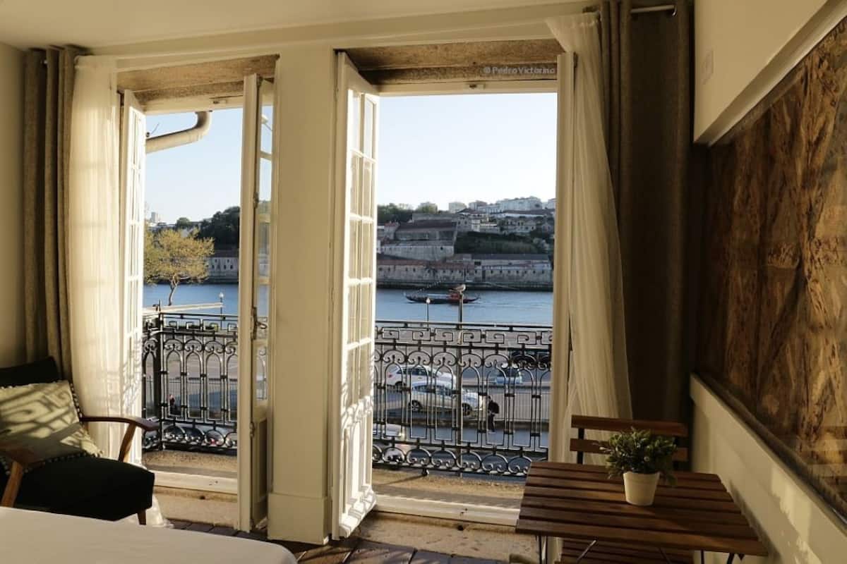 A room with a balcony overlooking a river and historic buildings.