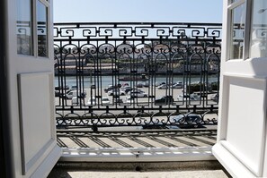 Une vue à travers une grille métallique ornée de motifs, qui donne sur un parking où se trouvent des voitures, avec une étendue d'eau en arrière-plan.