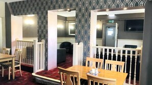 A restaurant with wooden tables and chairs, a patterned wall, and a red carpeted floor.