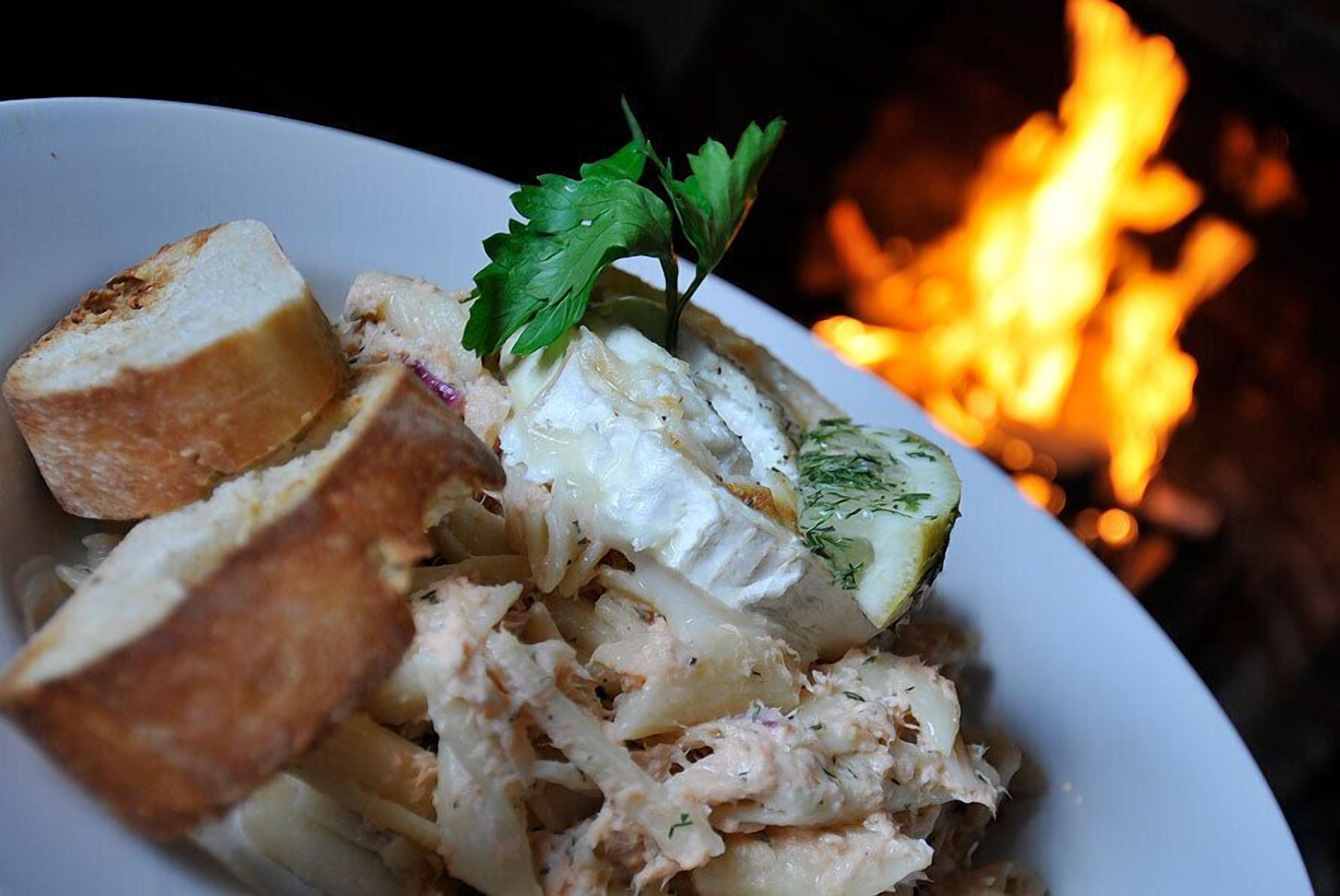 A plate of food with bread and a garnish, with a fire in the background.
