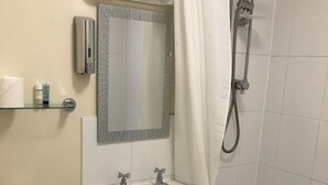 A bathroom with a toilet, sink, mirror, shower, and a glass shelf with toiletries.