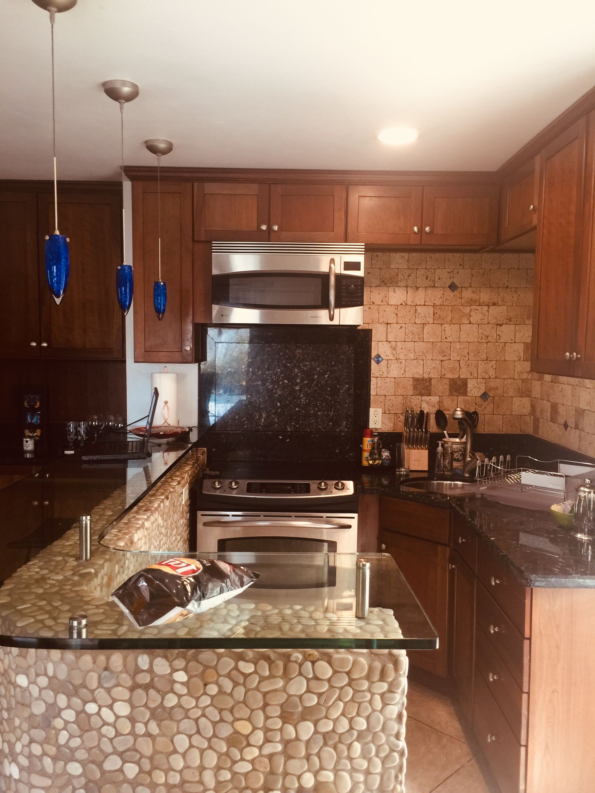 A modern kitchen with a granite countertop, stainless steel appliances, wooden cabinets, and a pebbled backsplash.