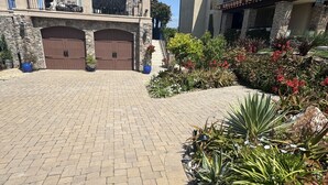 A driveway leading to a house with a stone facade, a garage, and a landscaped garden with various plants and flowers.