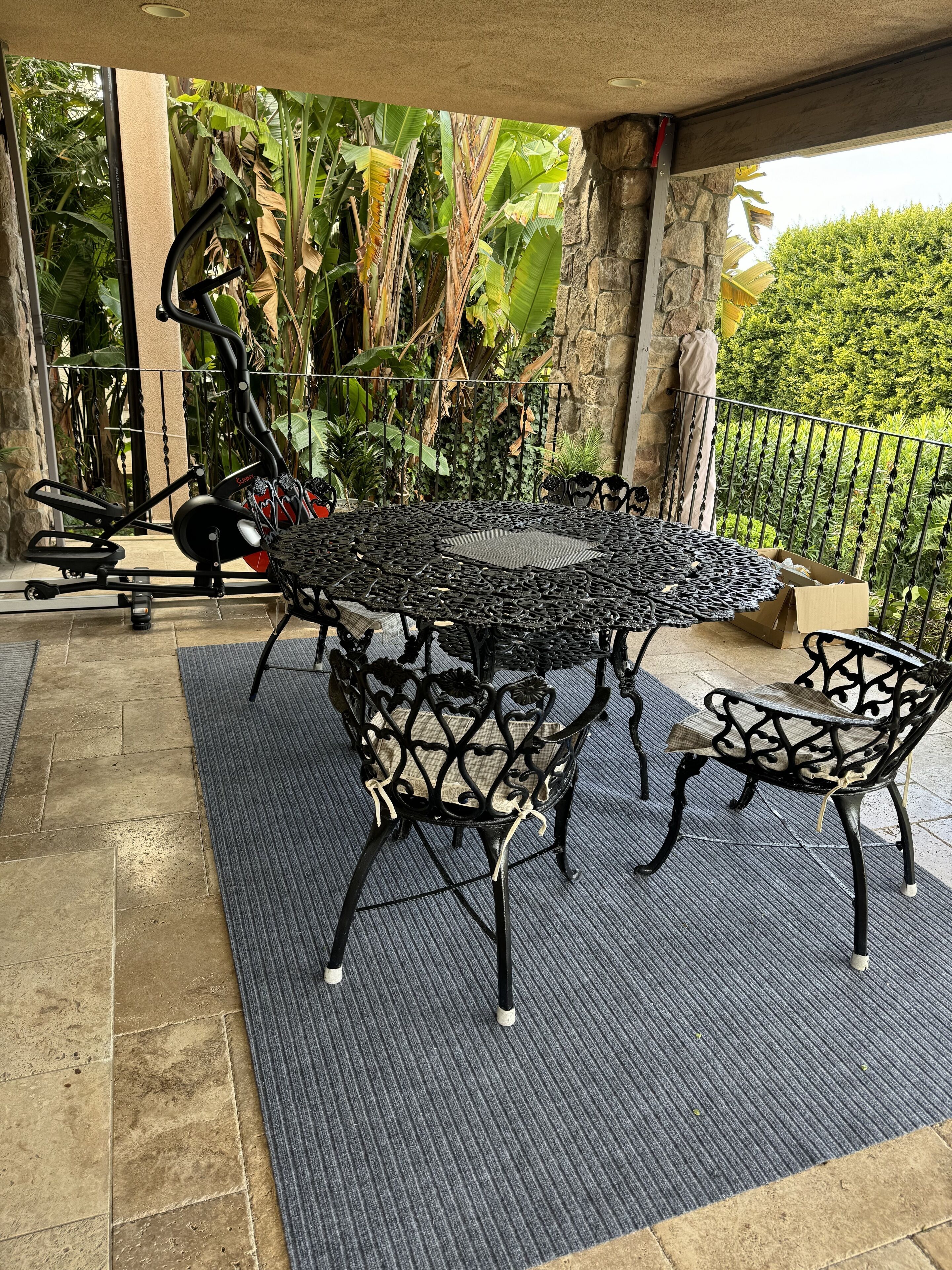 Eine Terrasse im Freien mit einem runden Metalltisch, umgeben von Stühlen, einem stationären Ergobicycle und einer Wand aus Stein.