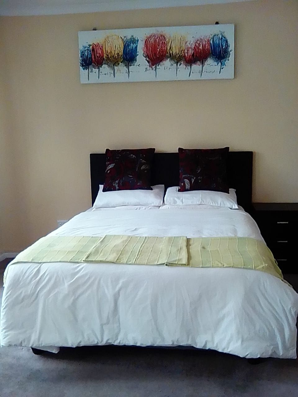 Een bed met witte lakens, twee dongekleurde kussens en een schilderij erboven.