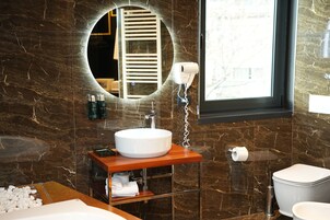 Un baño con pared de mármol, un espejo redondo, un lavamanos blanco, un secador de pelo y un inodoro.