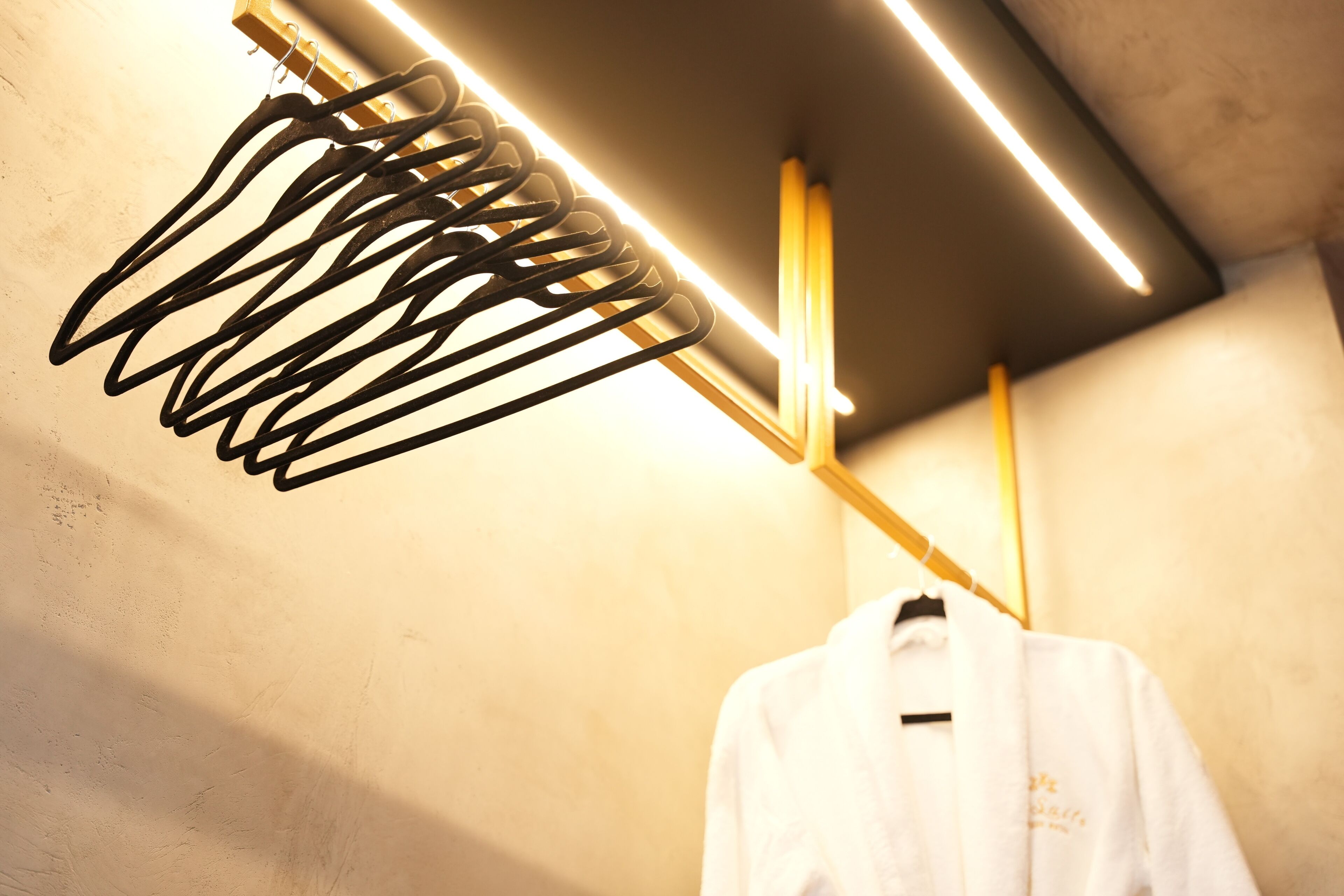 A white robe hanging on a wooden rack in a room with a concrete wall and a modern light fixture.