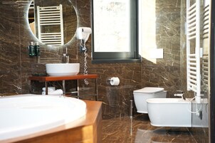 Un baño moderno con un espejo ovalado grande, un lavabo blanco, una bañera independiente y un inodoro.