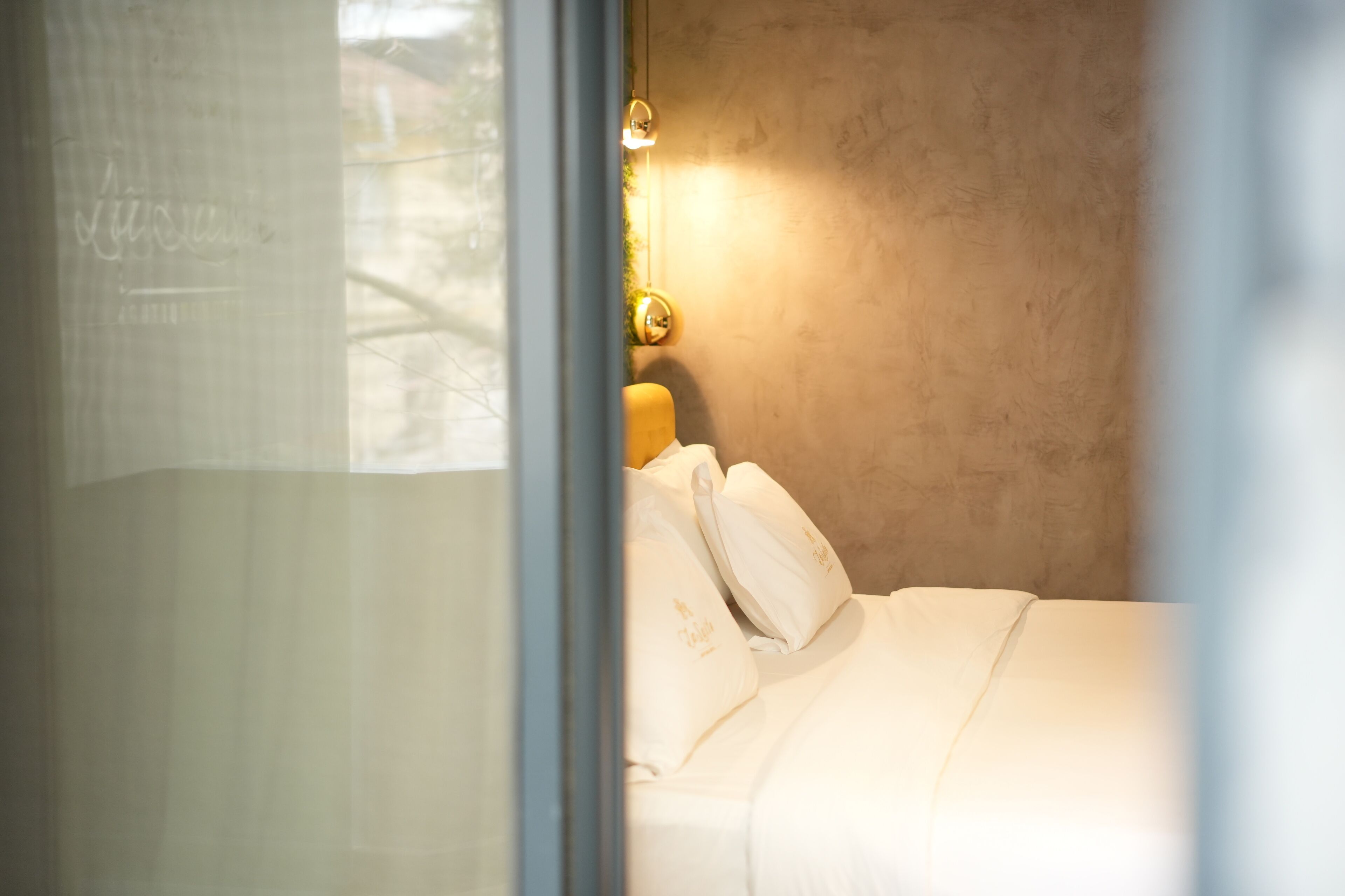 Una cama con ropa de cama blanca y una lámpara fijada a la pared.