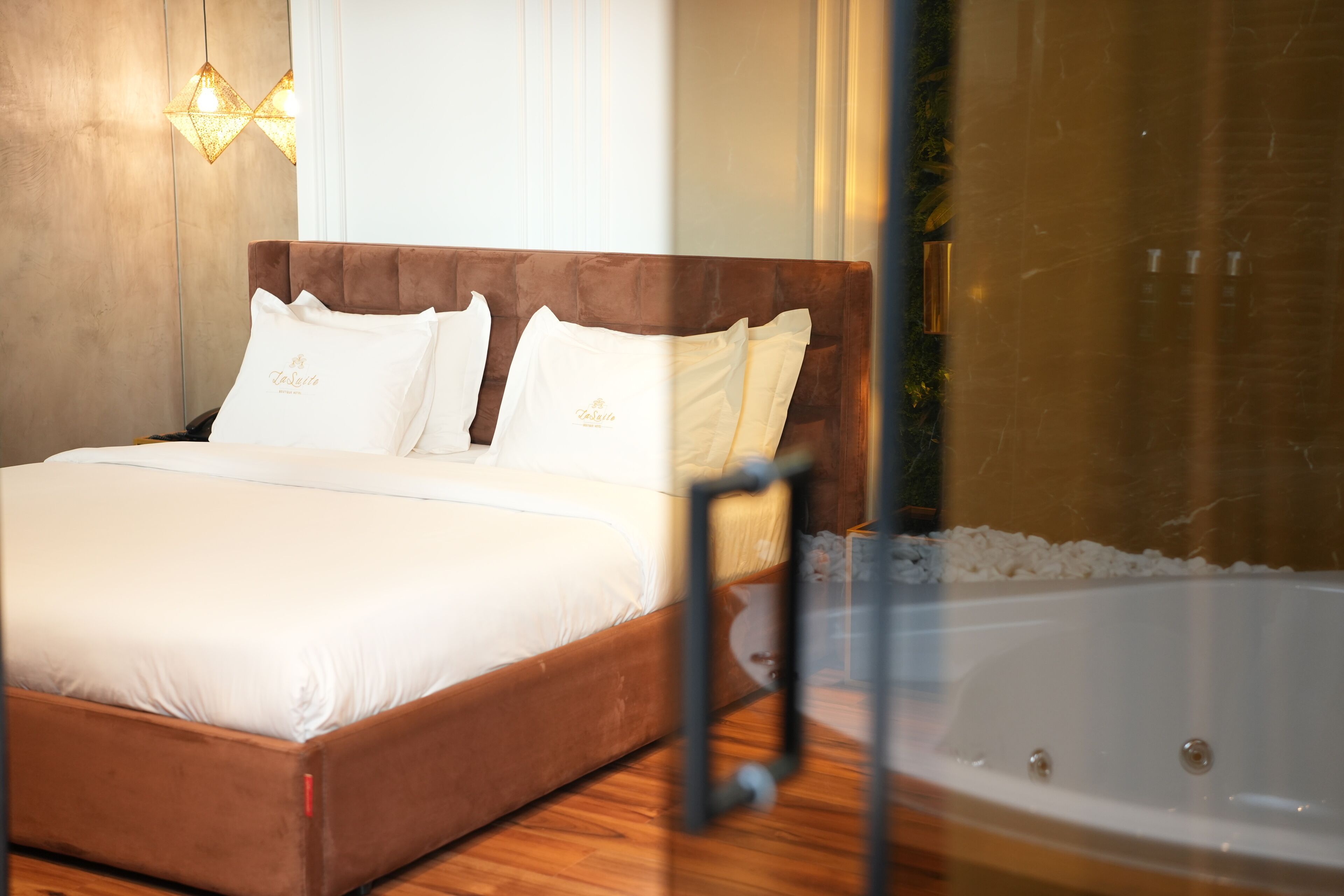 A bedroom with a large bed, a glass-enclosed bathtub, and a wooden floor.