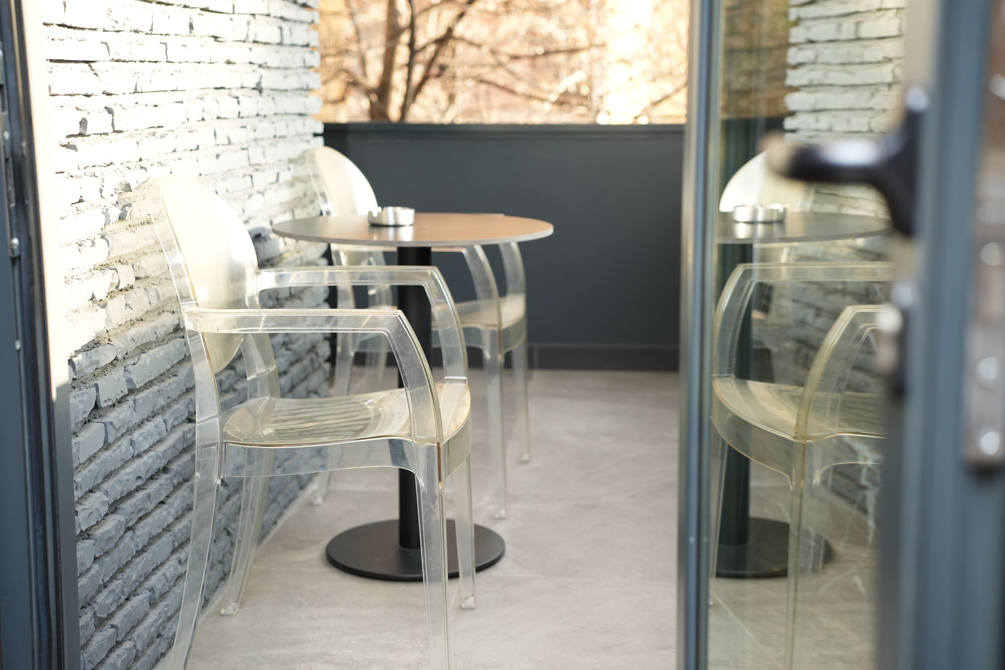 A seating area with transparent chairs and a round table, set against a brick wall with a window view.