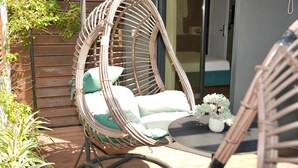 A wicker chair with cushions, a small table with a plant, and a wooden deck. - La Suite Boutique Hotel (Tirana)