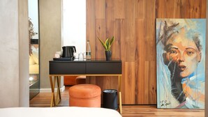 A modern hotel room with a wooden wall, a black desk with a plant, and a painting. - La Suite Boutique Hotel (Tirana)