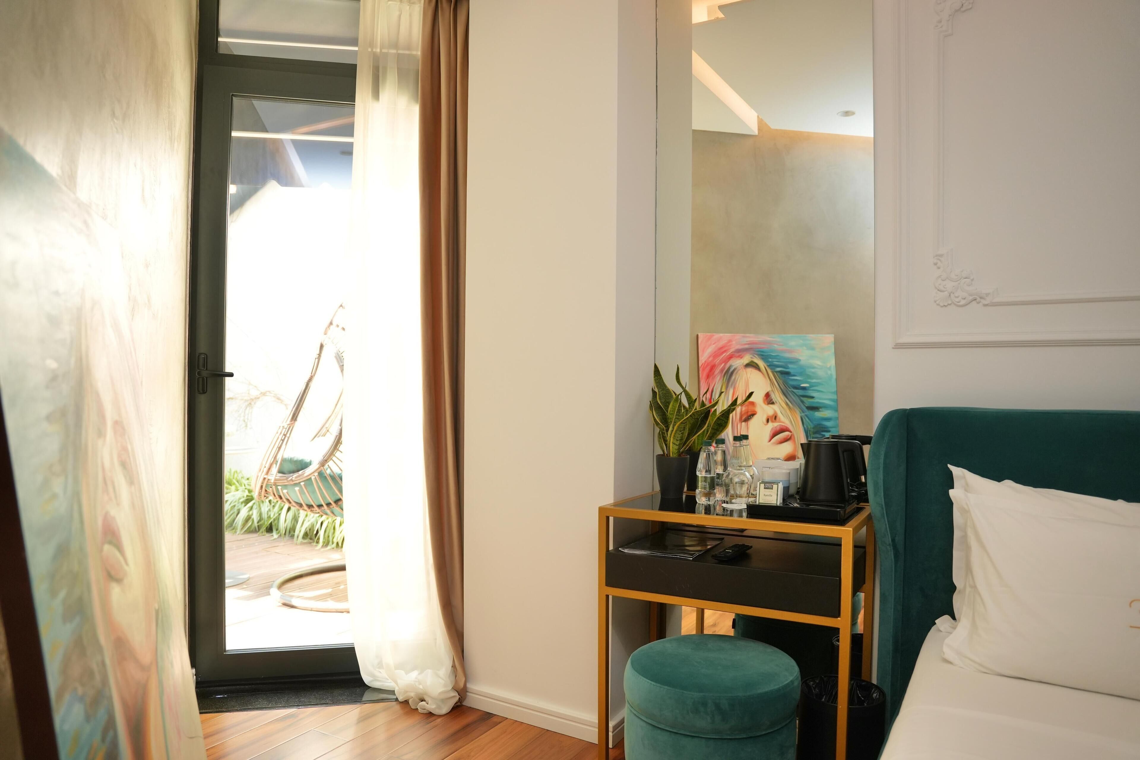A room with a bed, a desk with a plant, a painting, and a view of the outdoors.