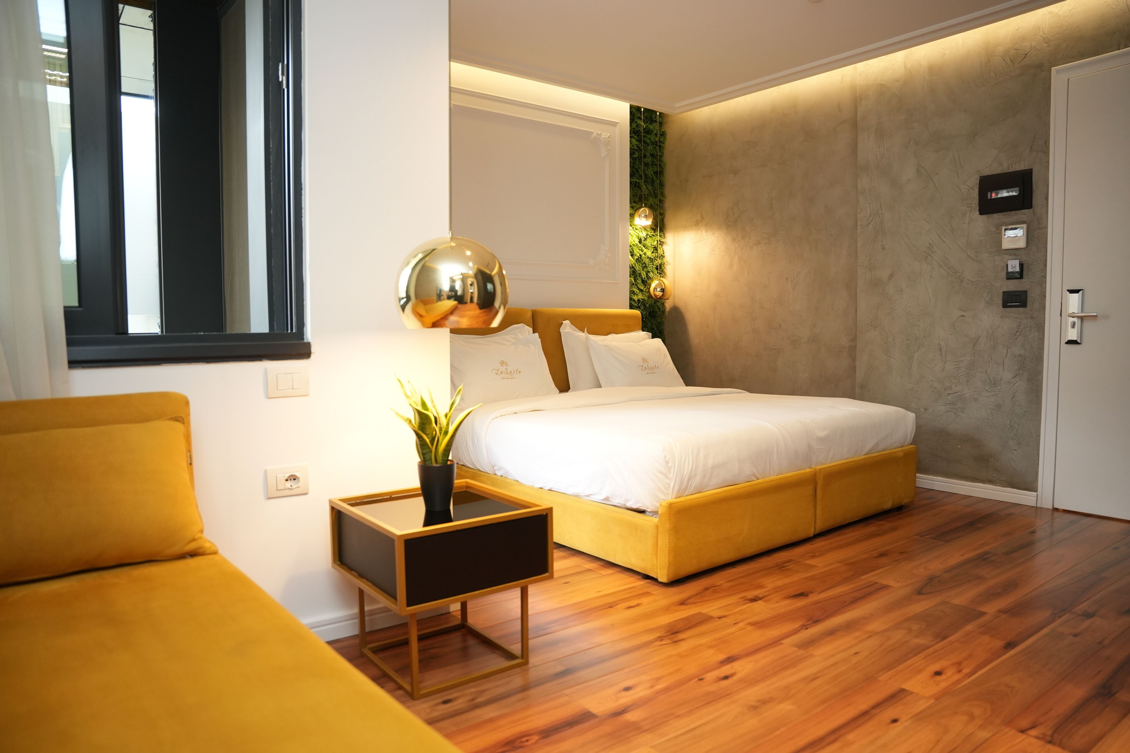 Une chambre à coucher moderne avec un grand lit, une petite table de chevet, une plante en pot et une fenêtre avec des stores.