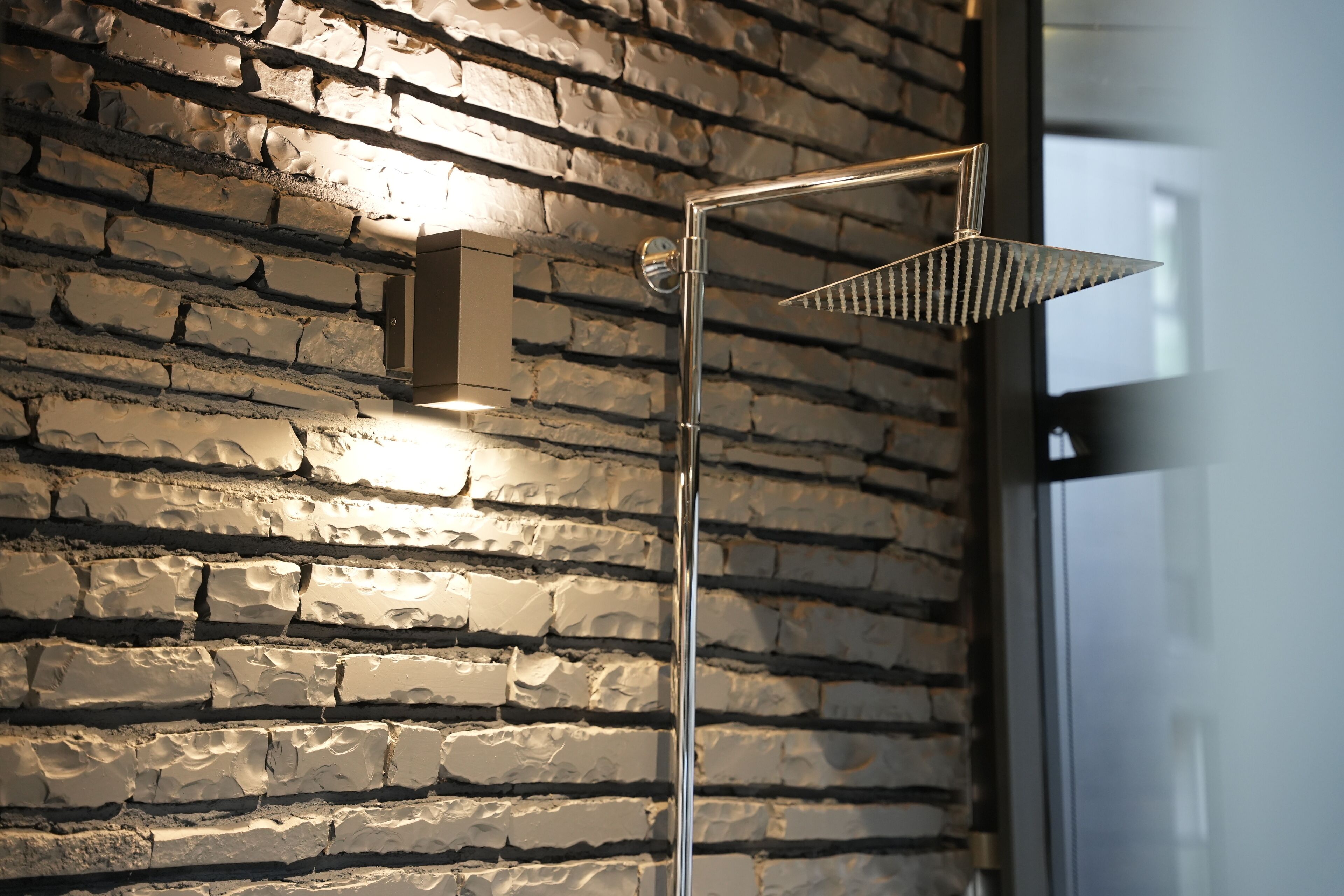 A modern shower with a metal frame and a textured wall behind it.