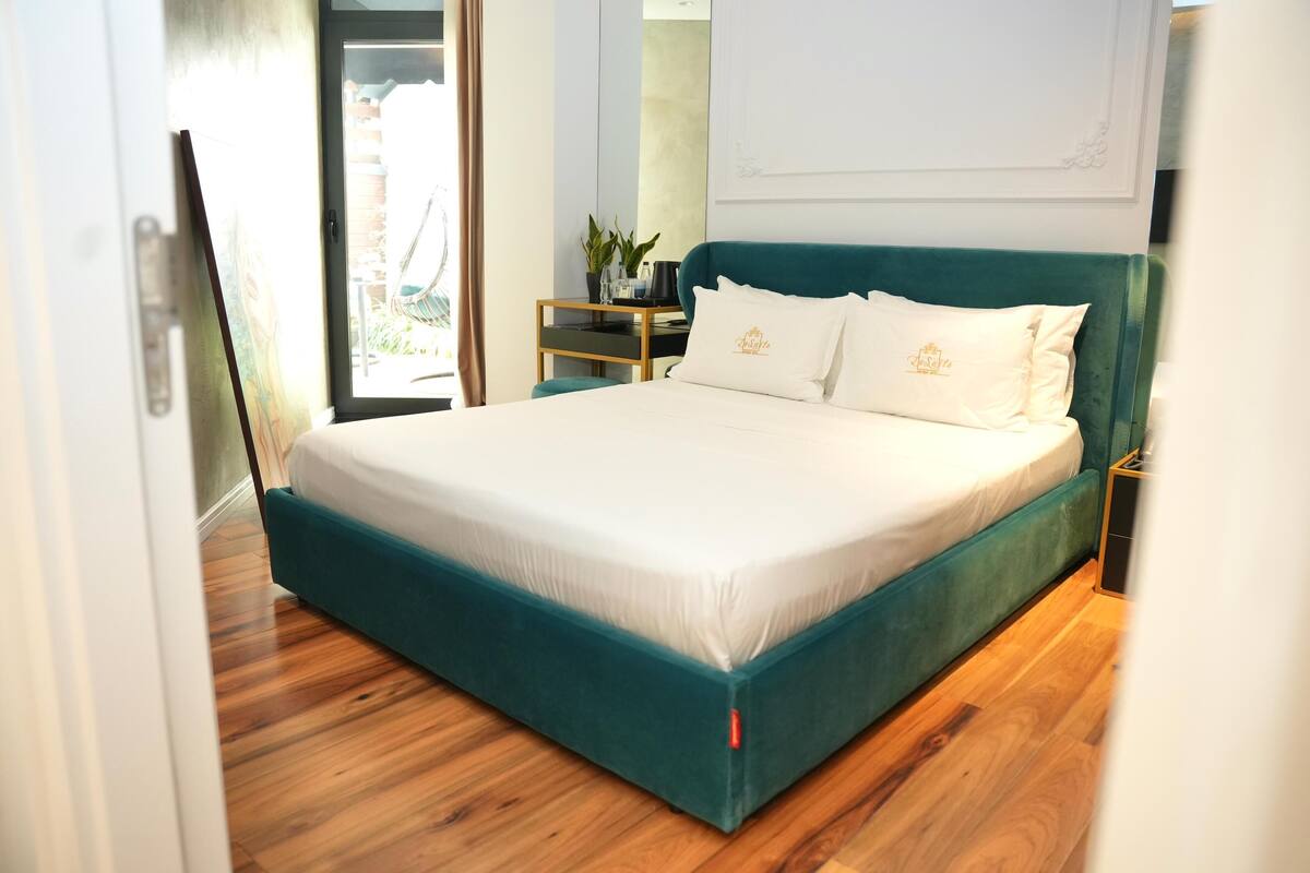 Une chambre à coucher moderne avec un lit de couleur turquoise, du linge de lit blanc et un plancher en bois.