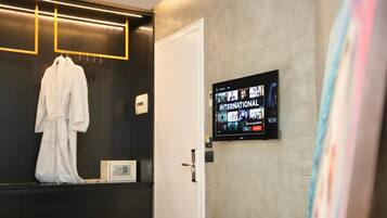 Habitación de hotel con un armario de color oscuro, una bata blanca colgada, un televisor mostrando opciones de películas y una puerta con manija.