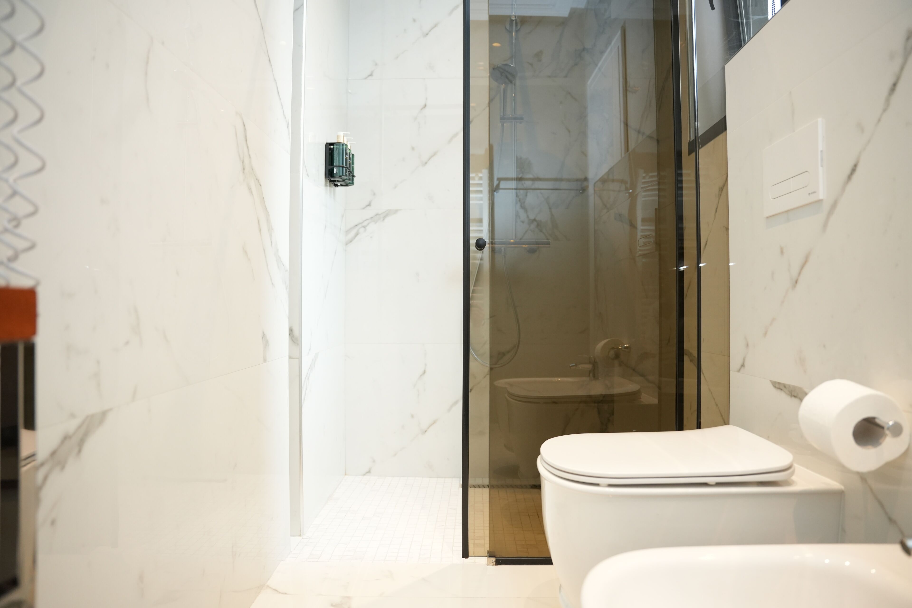 A modern bathroom with a glass-enclosed shower, a white toilet, and marble walls.