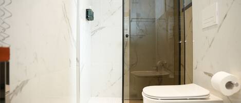 A modern bathroom with a glass-enclosed shower, a white toilet, and marble walls.