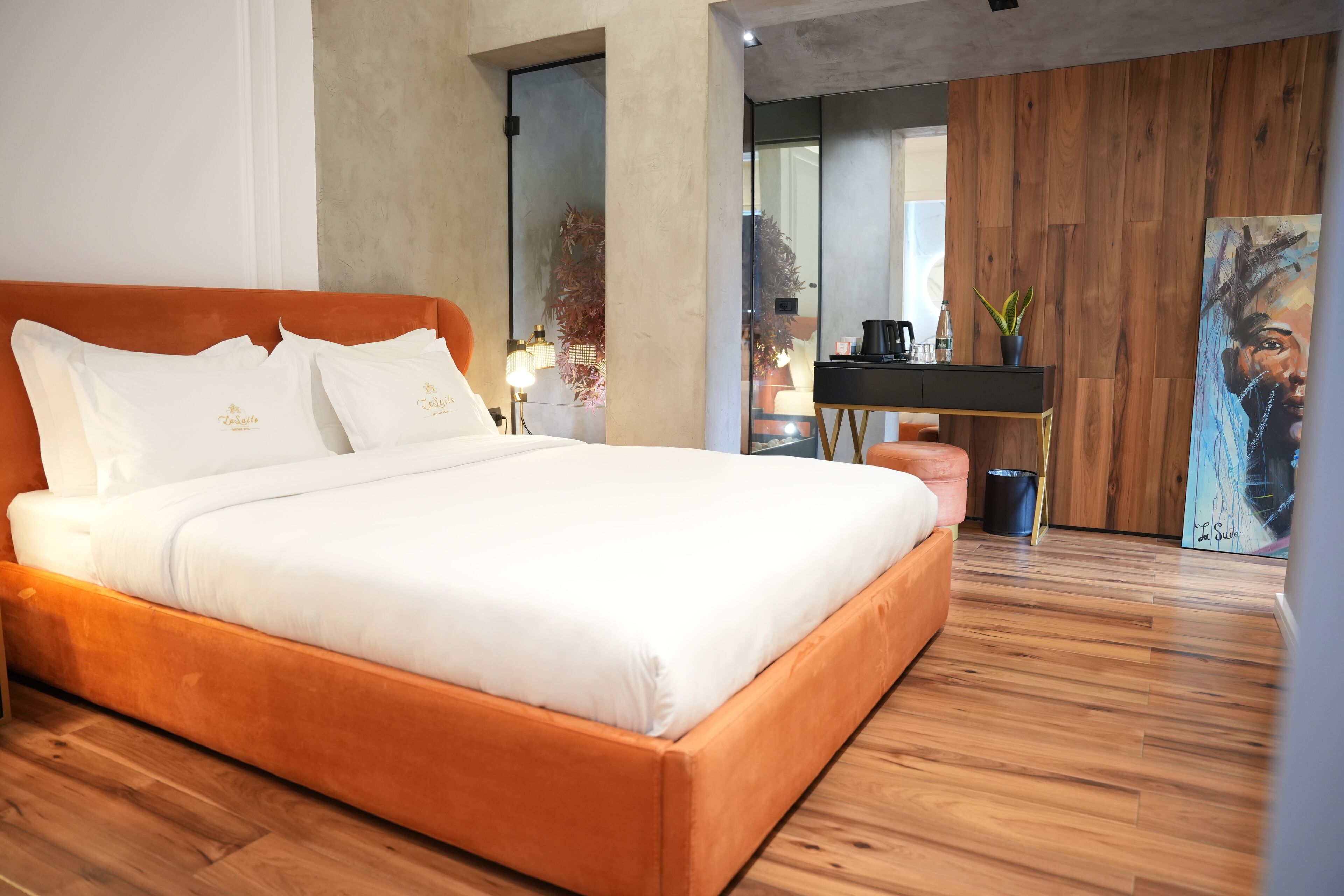 A modern bedroom with a wooden floor, a large bed with white bedding, a wooden headboard, and a painting on the wall.