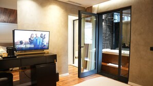A modern living room with a flat-screen TV displaying 'Ciudad Toxica' on Netflix, a coffee machine, a black sofa, and a wooden floor. - La Suite Boutique Hotel (Tirana)