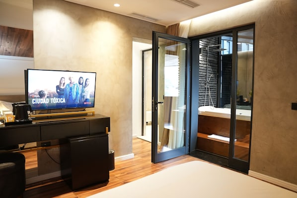 A modern living room with a flat-screen TV displaying 'Ciudad Toxica' on Netflix, a coffee machine, a black sofa, and a wooden floor. - La Suite Boutique Hotel (Tirana)