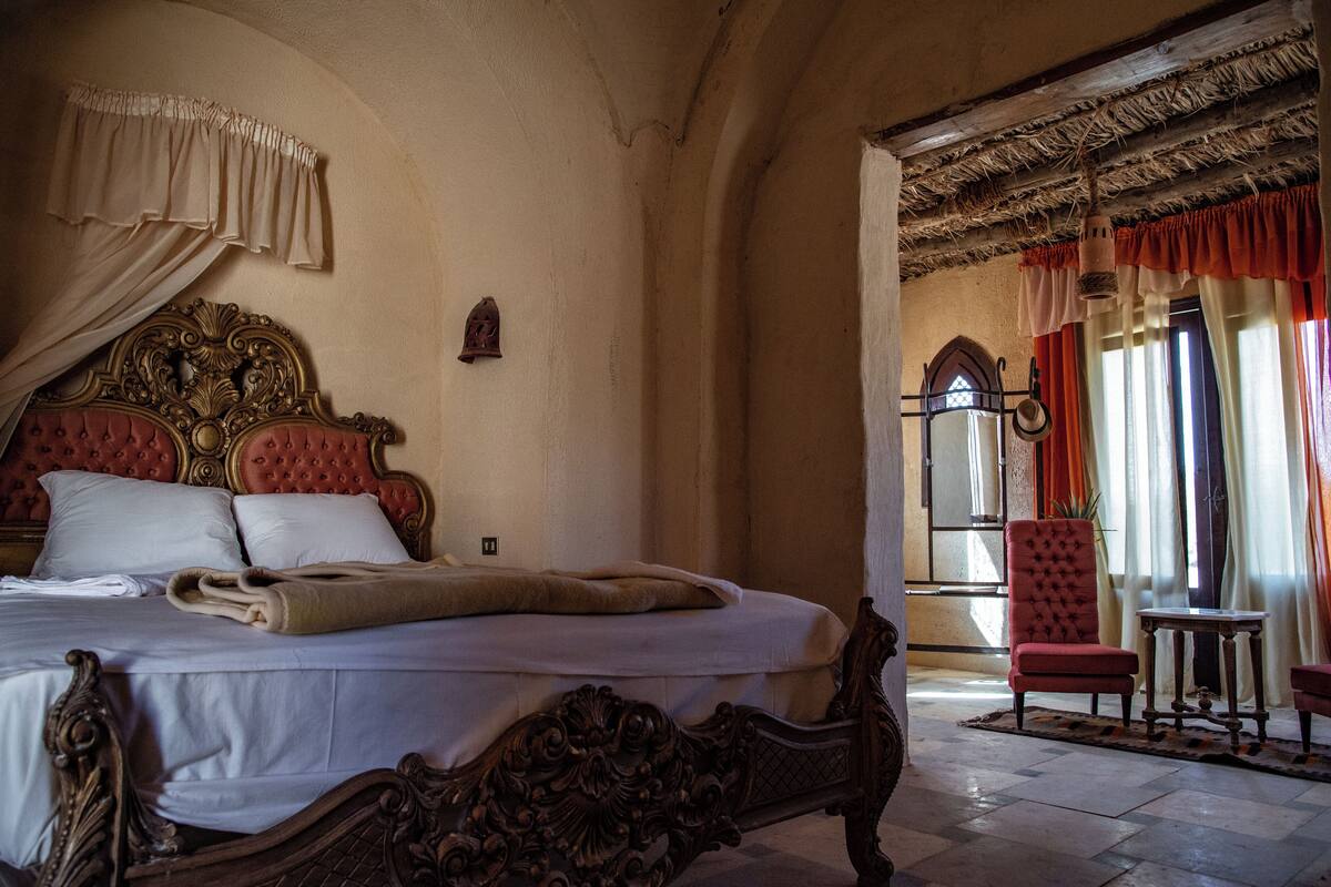 A bedroom with a large bed, ornate headboard, and a red chair.