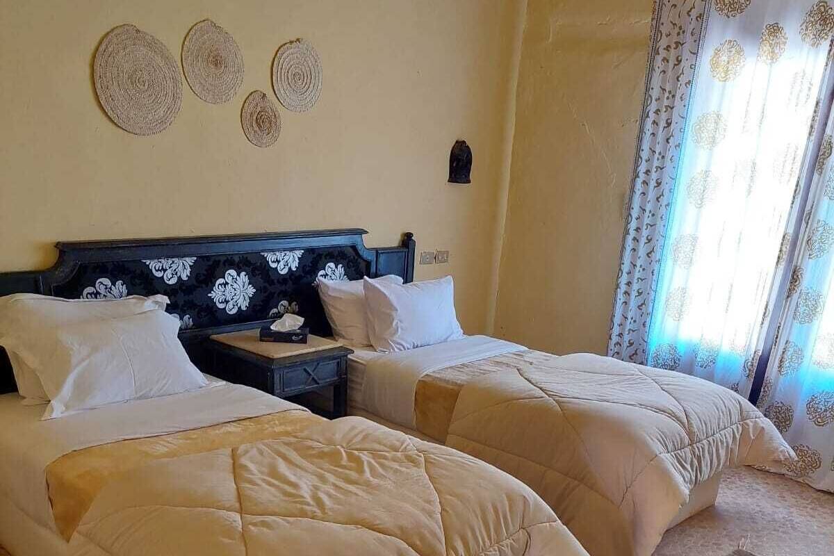 A bedroom with two beds, a nightstand, a wall clock, and a window with curtains.