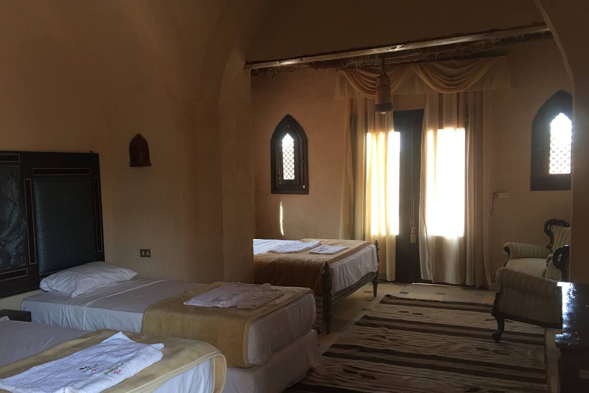 A hotel room with two single beds, a sofa, a chair, and a large window with curtains.