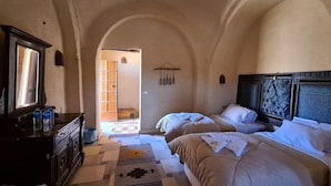 Een kamer met twee bedden, een kaptafel en een brede, gebogen deuropening naar een andere kamer.