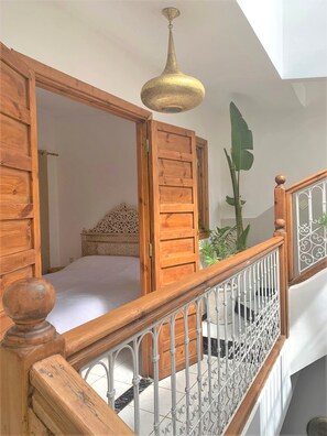 Un escalier avec des rampes en bois et une balustrade en métal, menant à une chambre à coucher équipée d’un lit et d’une tête de lit décorative.