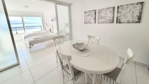 Una habitación moderna con una decoración blanca, una mesa redonda para comer, sillas blancas y un gran ventanal con vistas al mar.