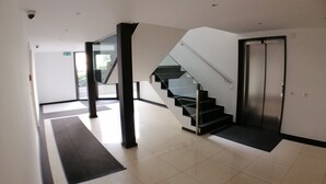Un interior moderno con una escalera de cristal, piso de baldosas impecable y un par de ascensores.