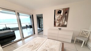 Una habitación de hotel moderna con una cama grande, un tocador blanco, una silla y un cuadro en la pared.
