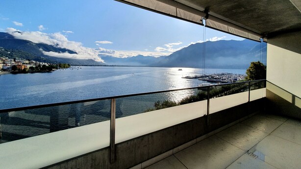 Un balcón con vistas a un lago, montañas y un puerto deportivo.
