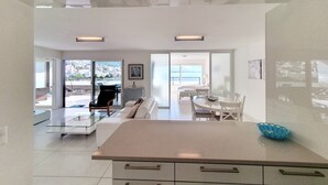 Una cocina moderna con una isla central, una zona de comedor con una mesa y sillas blancas, y una sala de estar con un sofá y una mesa de centro.