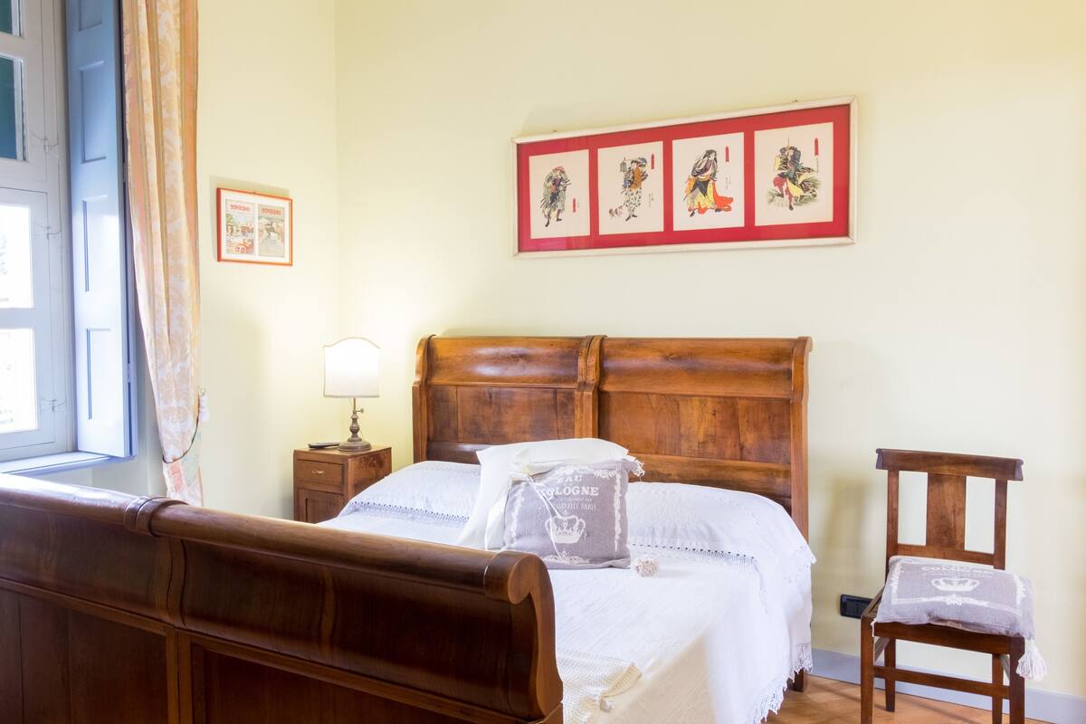 Un dormitorio ordenado con una cama de madera, una mesita de noche con lámpara y una silla.