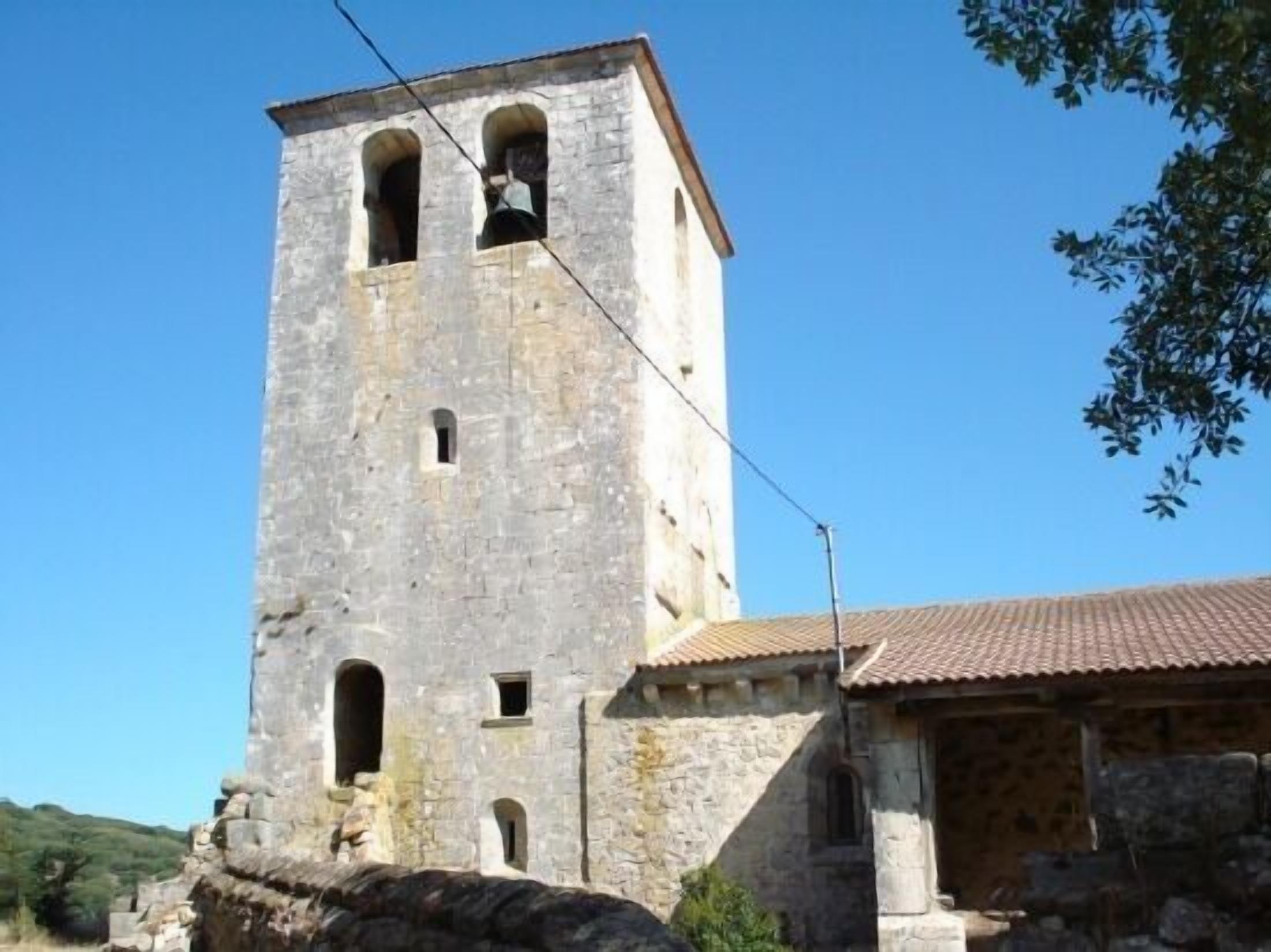 A stone tower with arched windows and a bell, attached to a building with a tiled roof.