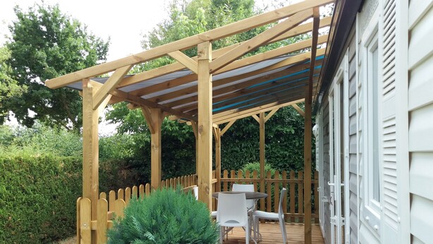 Une pergola en bois avec un toit, une petite table et deux chaises, installée dans un coin du jardin.
