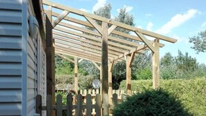 Une structure de pergola en bois, avec une clôture en bois à l’avant, qui mène à une zone abritée.