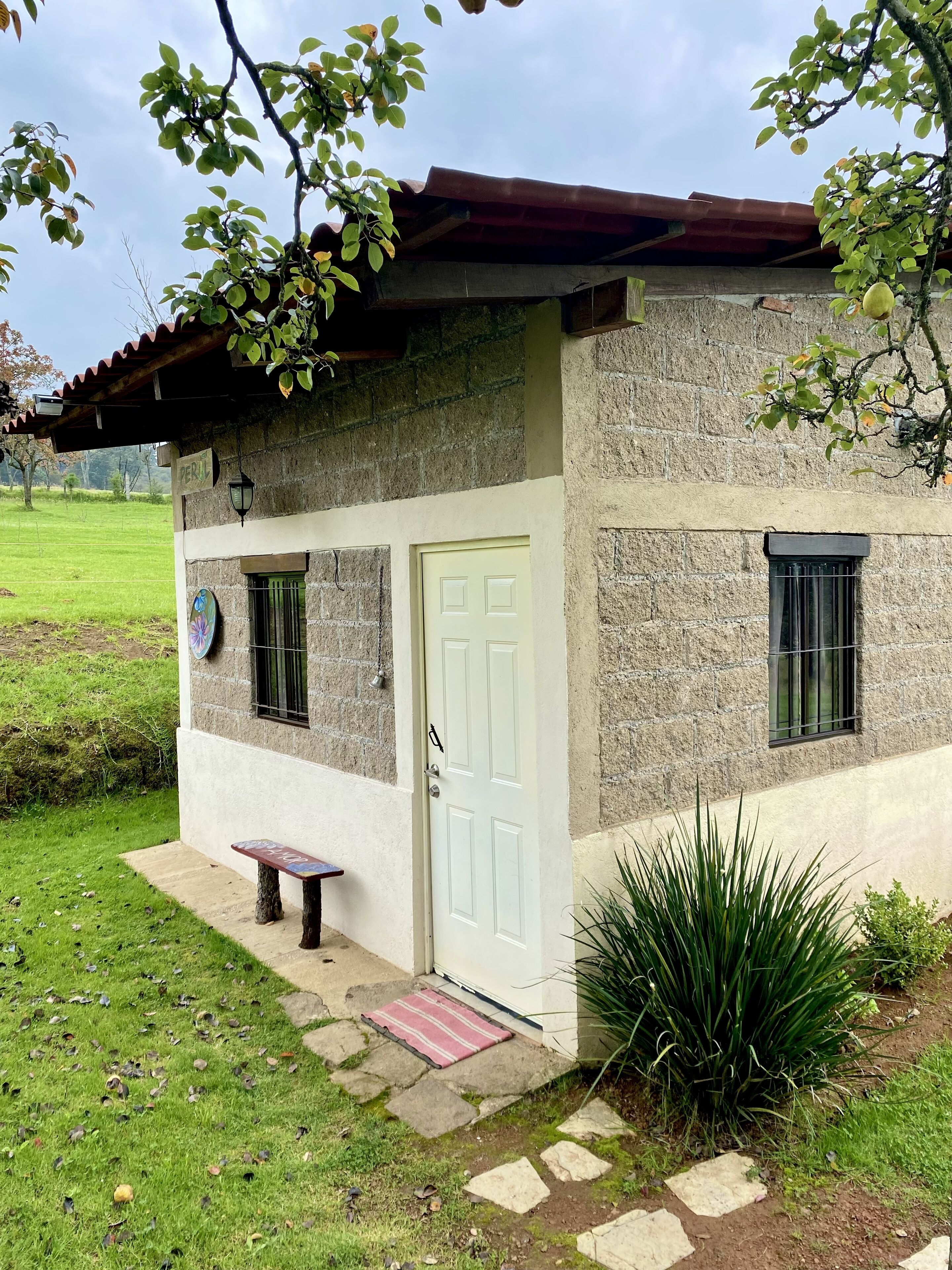 A rustic stone house with a white door, a small bench, and a garden with a stone pathway.